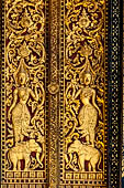 Wat Xieng Thong temple in Luang Prabang, Laos. Detail of a wooden door of the sim with gilded carvings on a red background. 